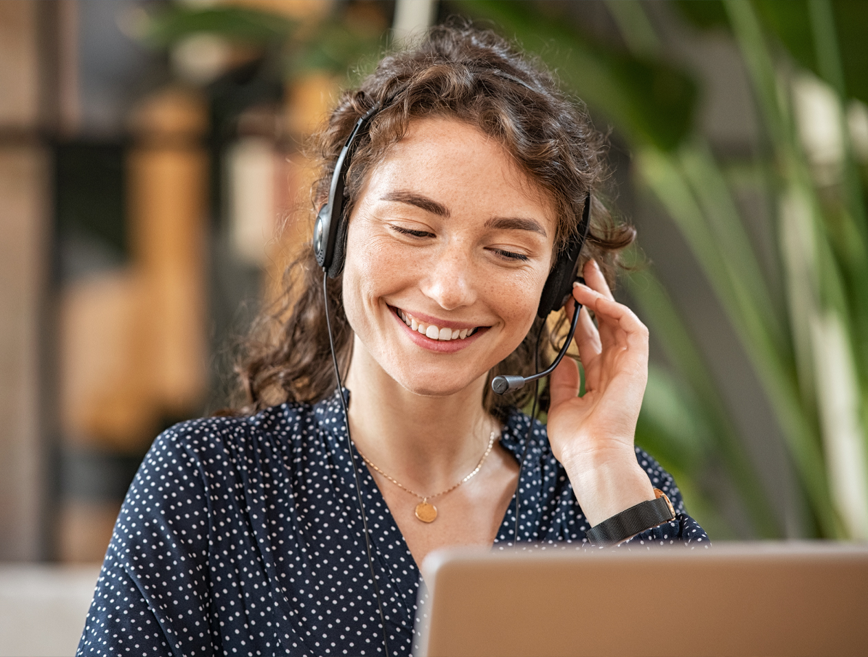 Frau vor Laptop sitzend mit Headset telefonierend